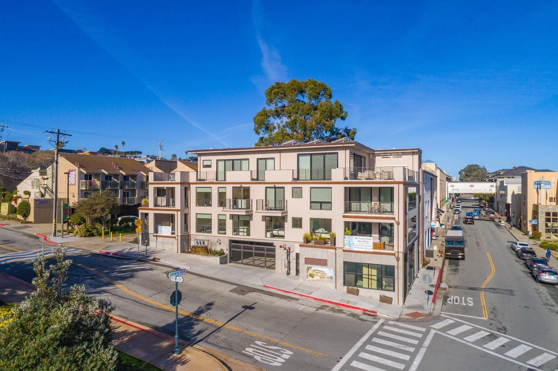 A multistory building with balconies on each floor, located at the corner of a street named Cannery Row, with other buildings and cars on the road. Clear blue sky overhead.