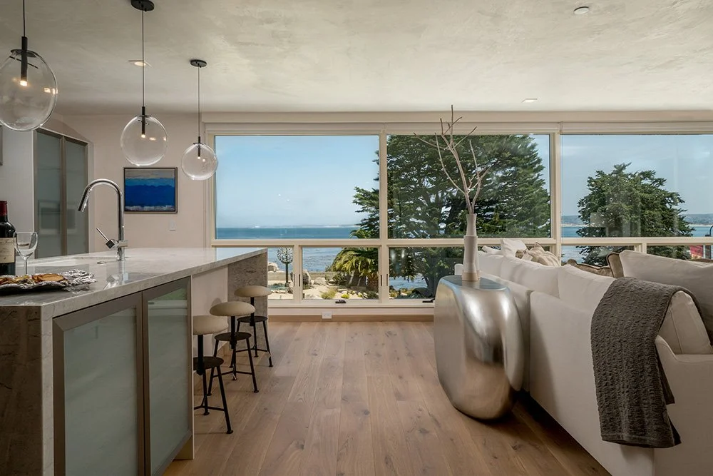 Living room with floor-to-ceiling windows overlooking the ocean, modern furniture, and minimalist decor.