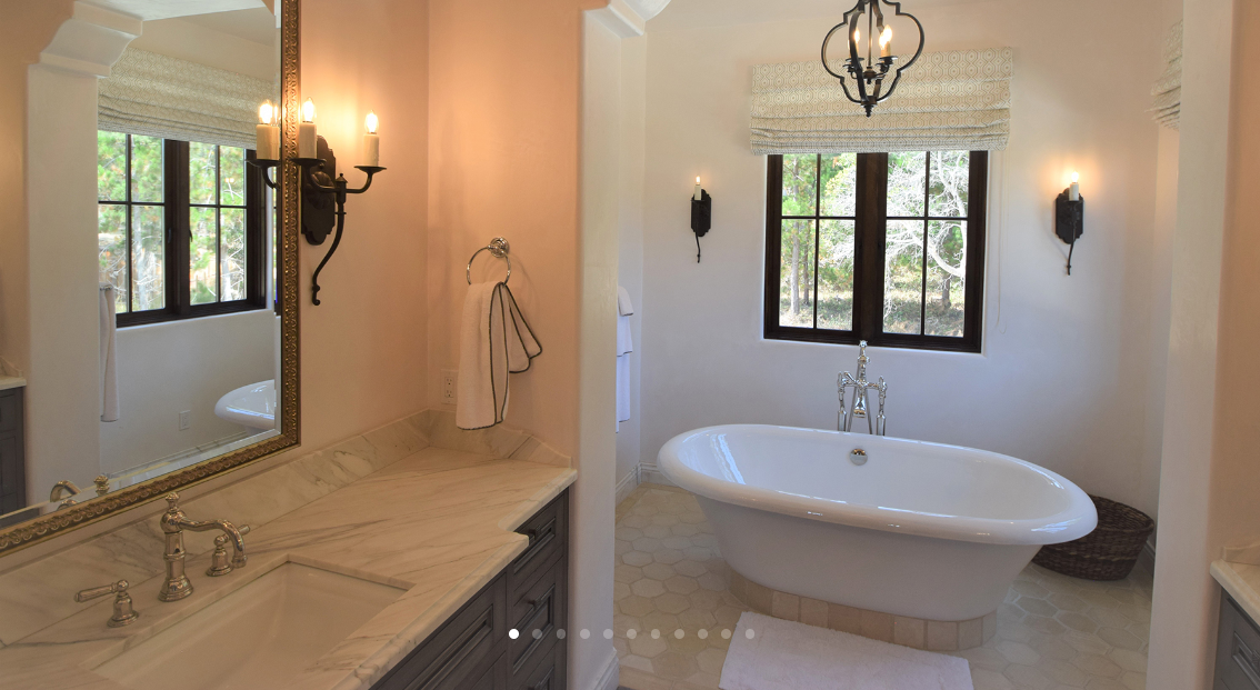 Bathroom with a clawfoot bathtub, two windows, wall sconces, a marble countertop with a sink, and a mirror.