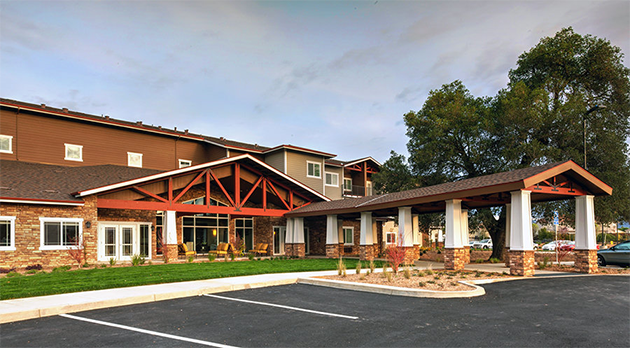 Exterior view of a modern multi-story senior living or assisted living facility with a landscaped entrance and parking lot.