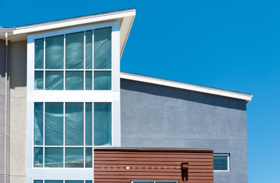 Close-up of a modern building with large glass windows, blue sky, and a mix of gray and brown exterior materials.