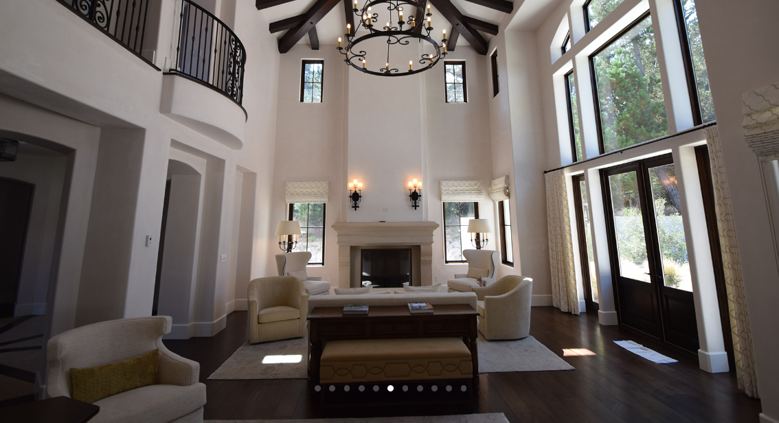 Spacious living room with high vaulted ceiling with dark wooden beams, large windows, fireplace, and elegant furniture.