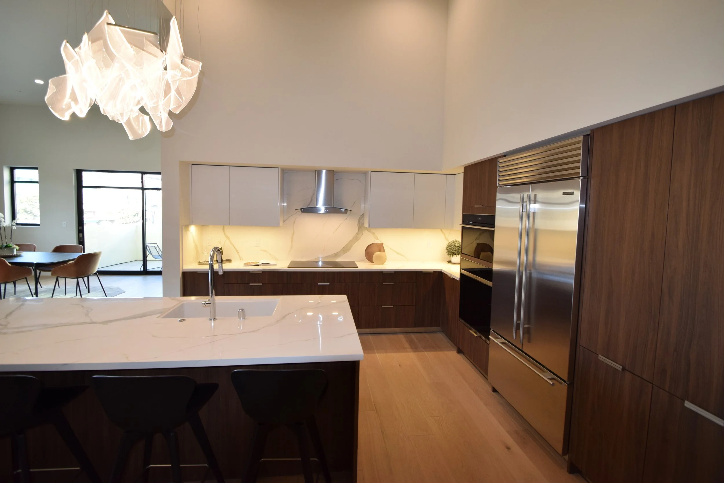 Modern kitchen with white marble island, dark wood cabinets, stainless steel appliances, and geometric chandelier lighting.