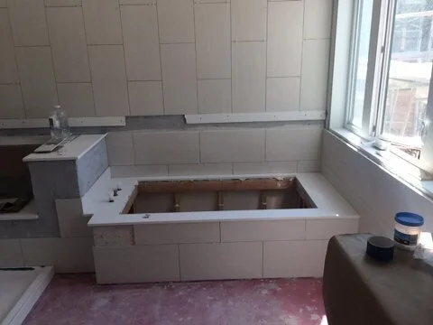 Empty bathroom with a built-in tub frame under construction, surrounded by white tiles and a large window.