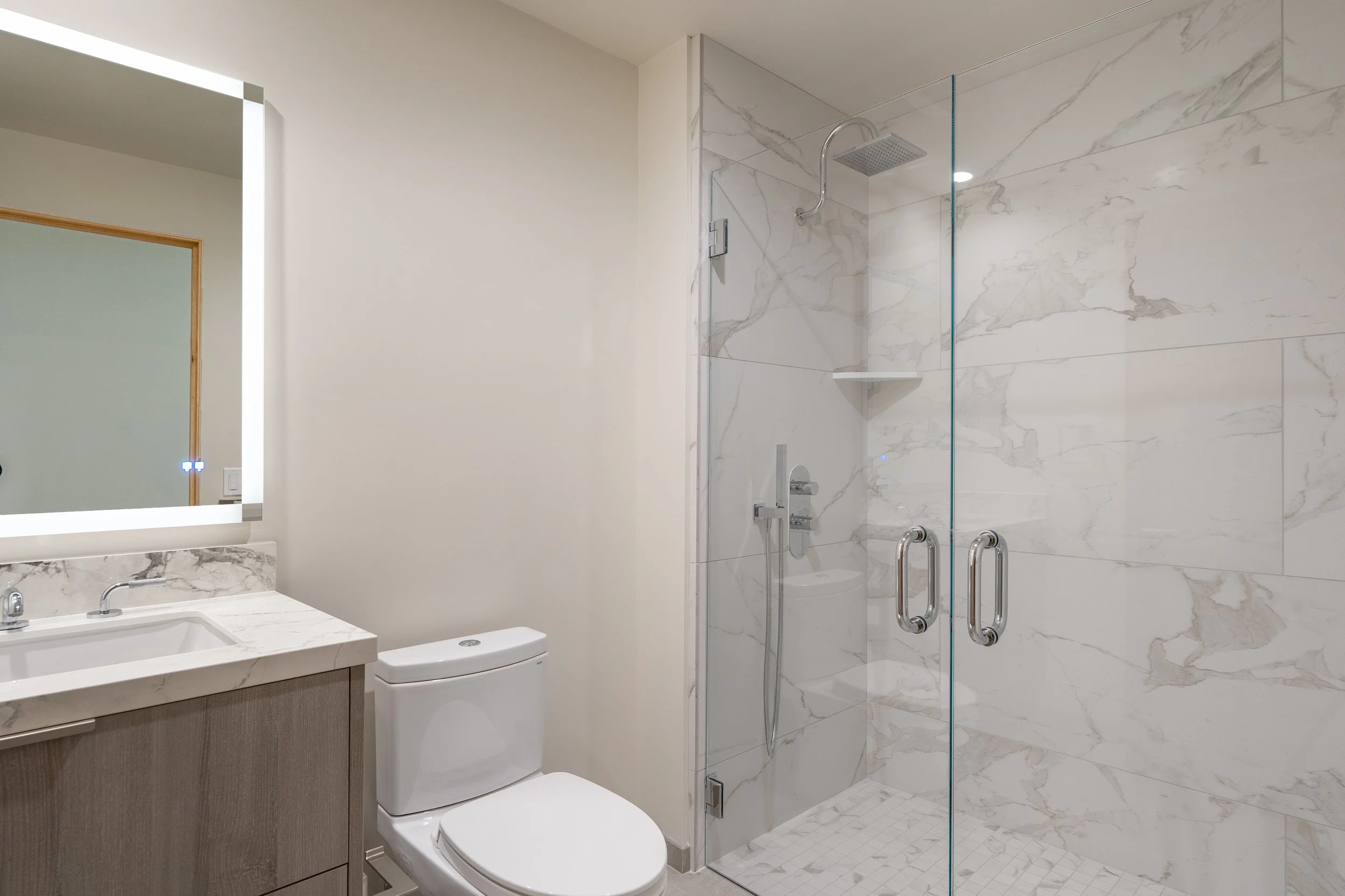 Modern bathroom with marble tile shower enclosure, white toilet, vanity with marble countertop, and mirror.