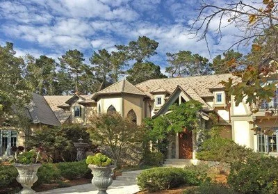 Large, elegant mansion with multiple gabled roofs, surrounded by well-maintained landscaping and trees.