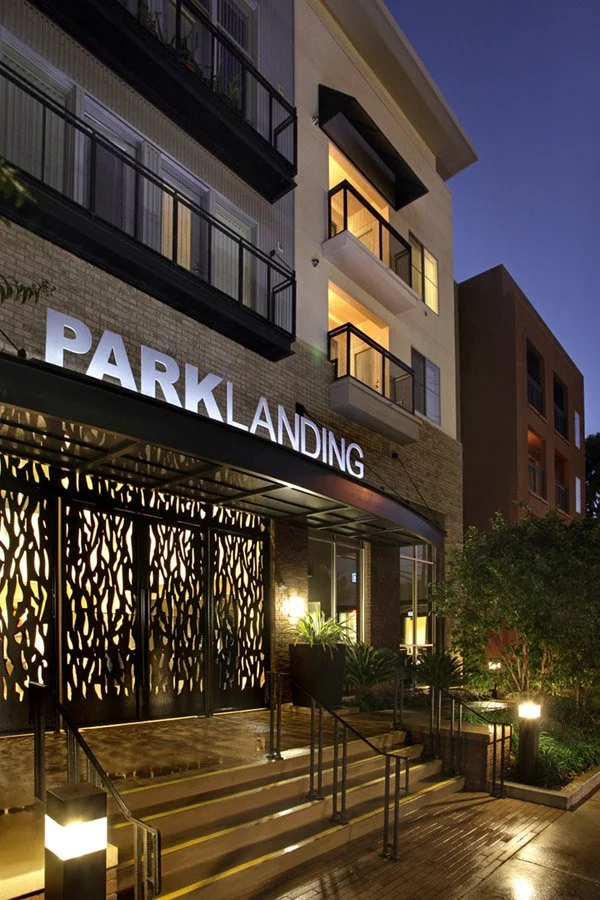 Modern multi-story building with balconies, illuminated entrance, and a sign reading 'PARK LANDING' at night.