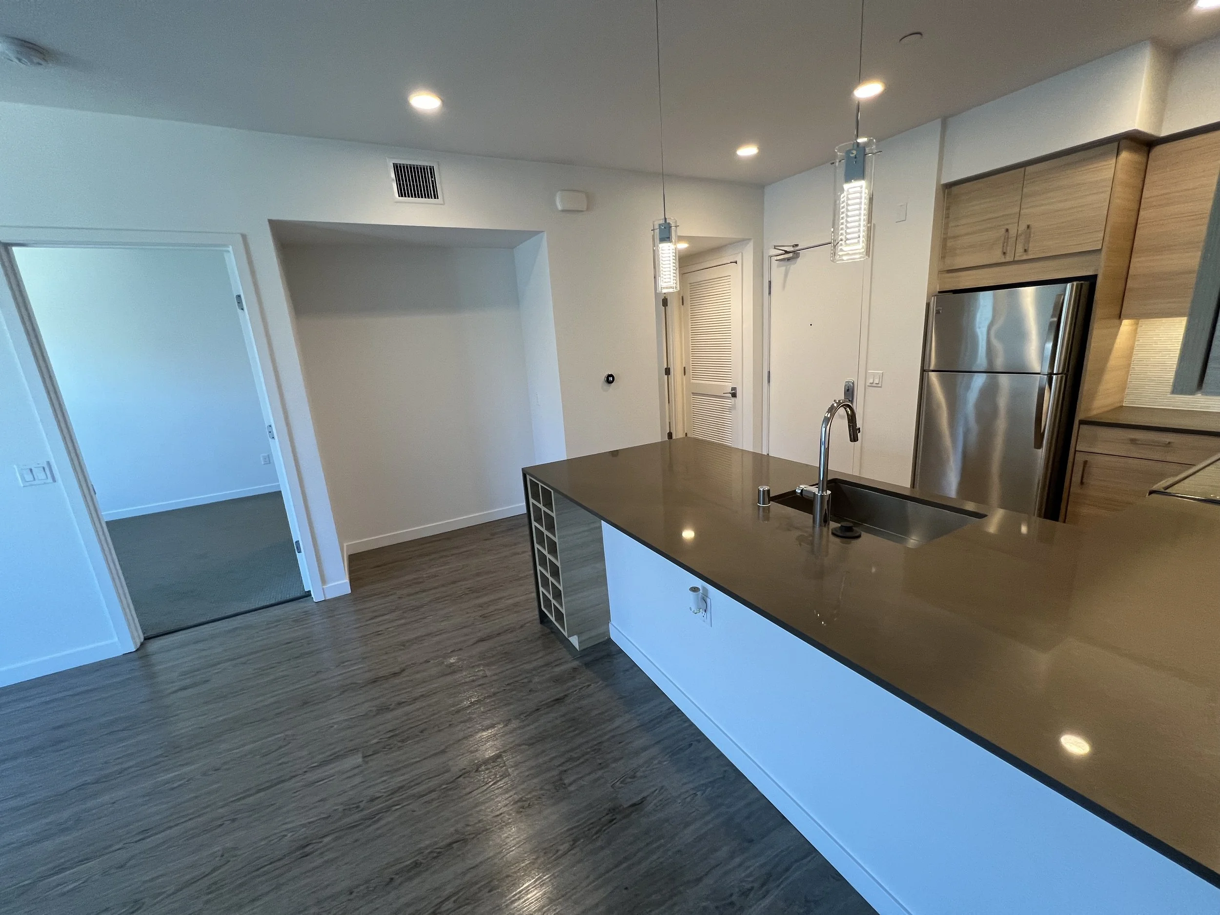 Modern kitchen with wood and white cabinets, stainless steel refrigerator, black countertop, and pendant lighting.