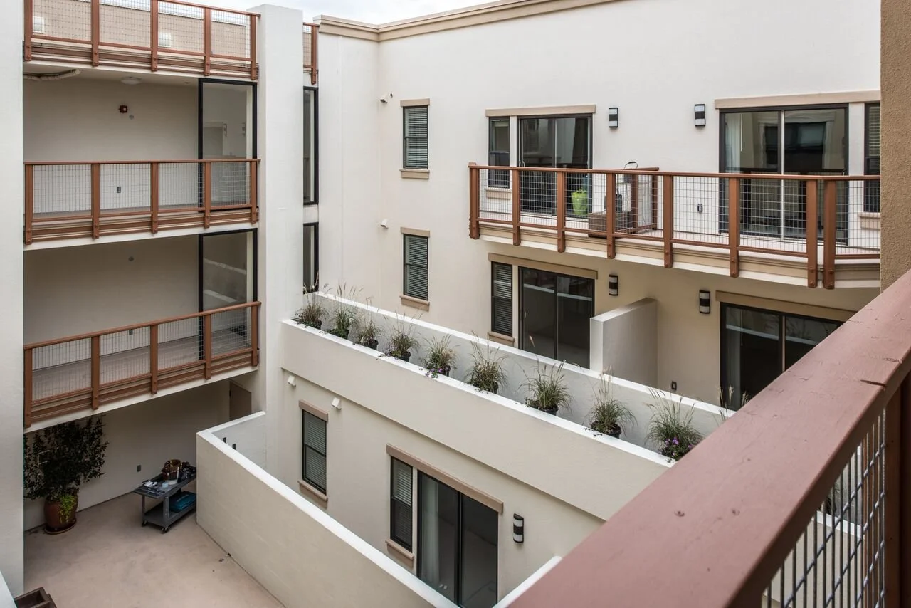 View of an outdoor apartment balcony courtyard with multiple levels, sliding glass doors, and potted plants