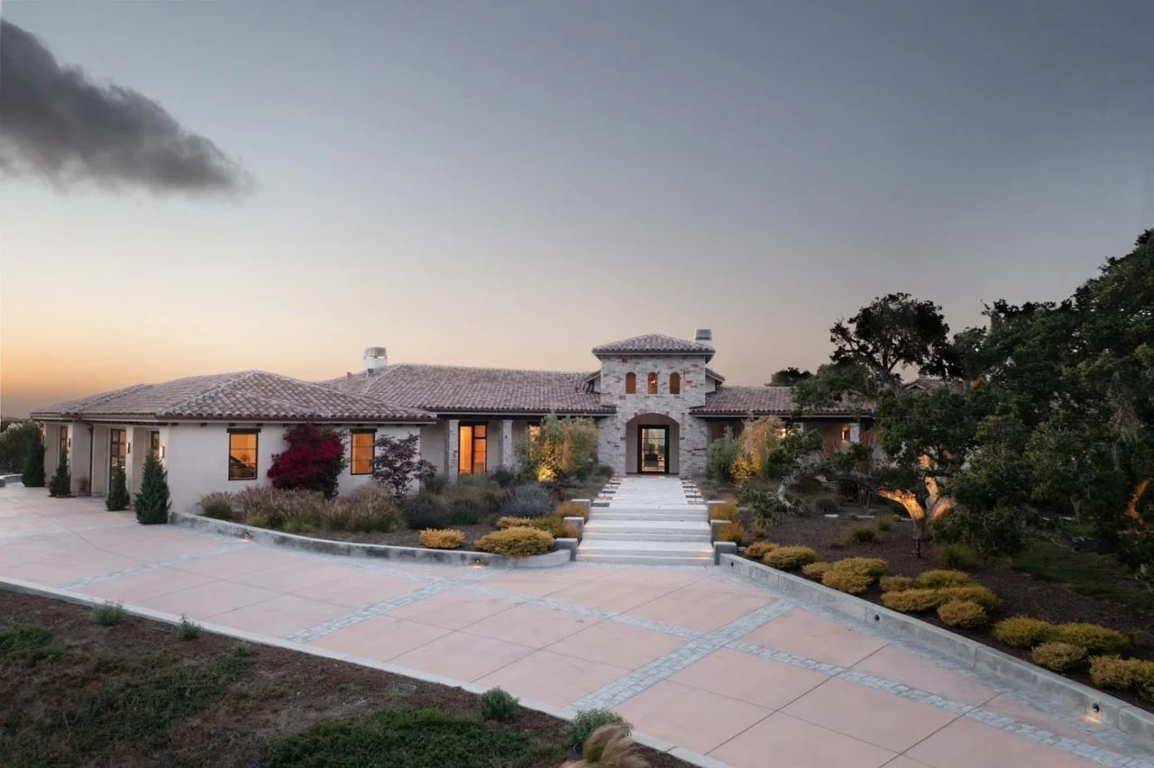 Front view of a large, luxurious house with well-maintained landscaping and a stairway leading to the entrance during dusk
