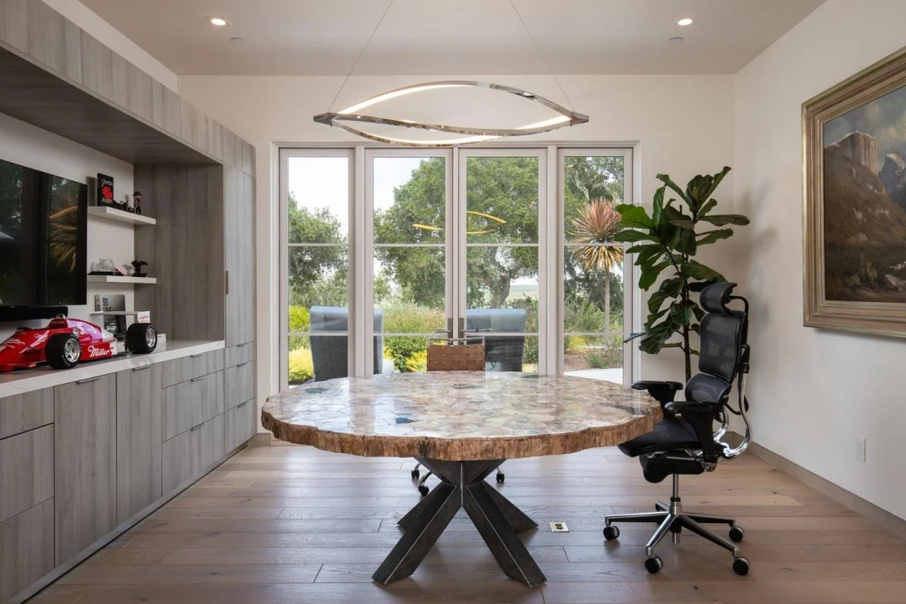 Modern home office with large marble-top table, black ergonomic chair, and view of outdoor garden through glass sliding doors.