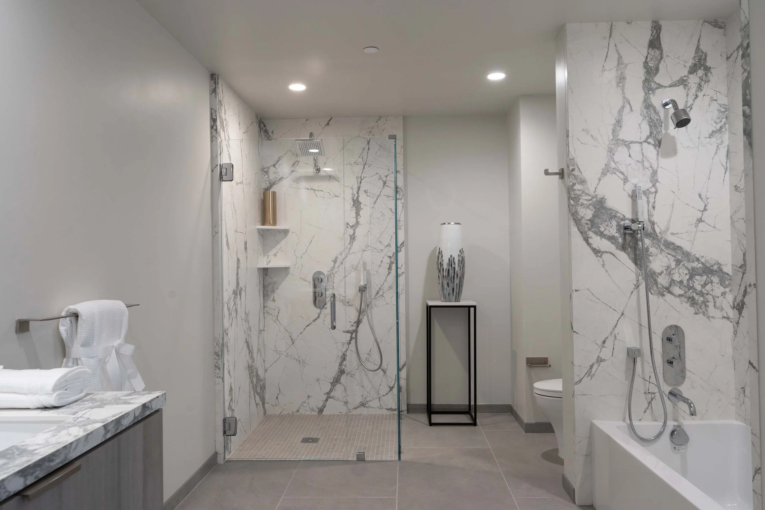 Modern bathroom with a marble shower, a floating vanity with towels, a decorative vase, and a toilet