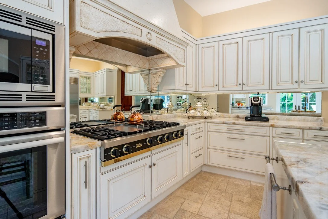 Bright white kitchen with beige countertops, stainless steel appliances, upper and lower cabinets, a gas stove, a microwave, and a coffee machine.