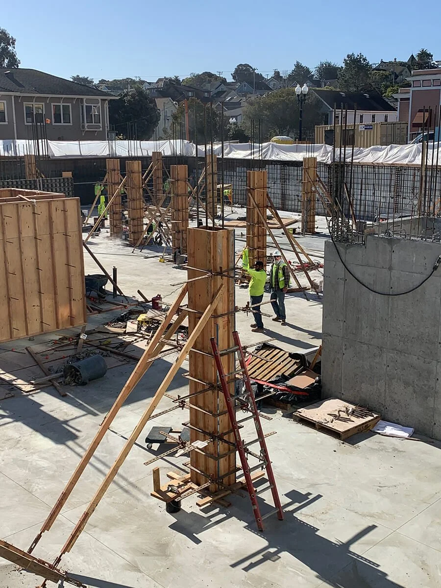 Construction site with workers and wooden framework, concrete walls, and building materials for a new structure.