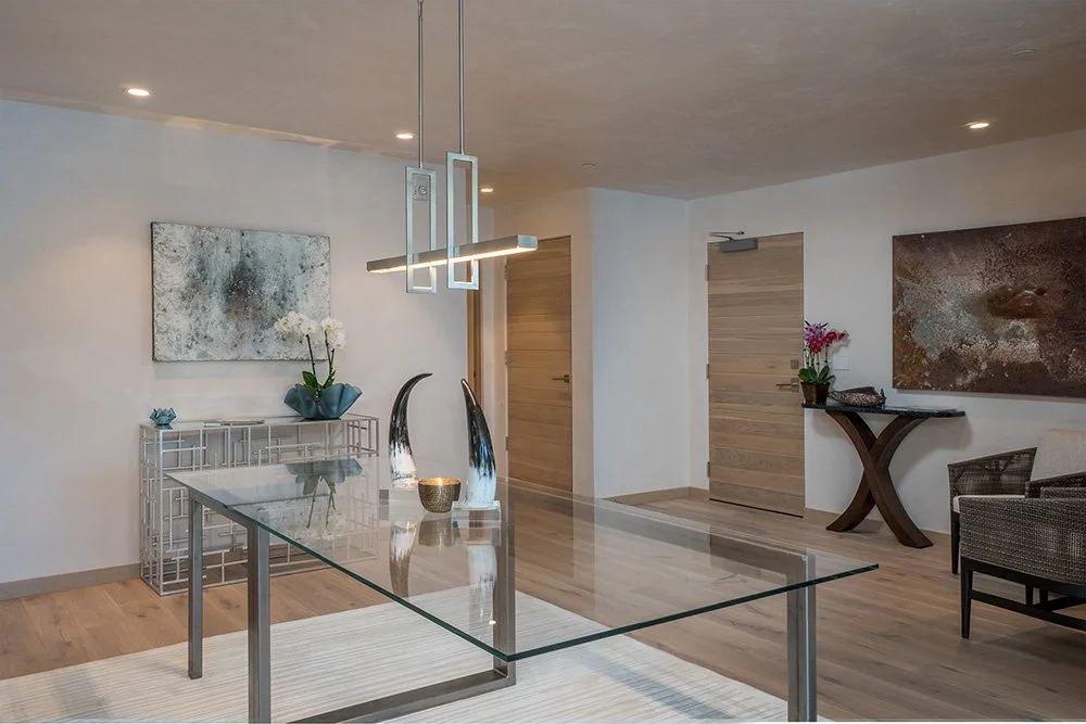 Modern dining room with a glass table, decorative vases, wall art, a floral arrangement, and seating area.