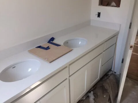 Bathroom vanity with a white countertop, two oval sinks, a closed cabinet under, and tools placed on the counter.
