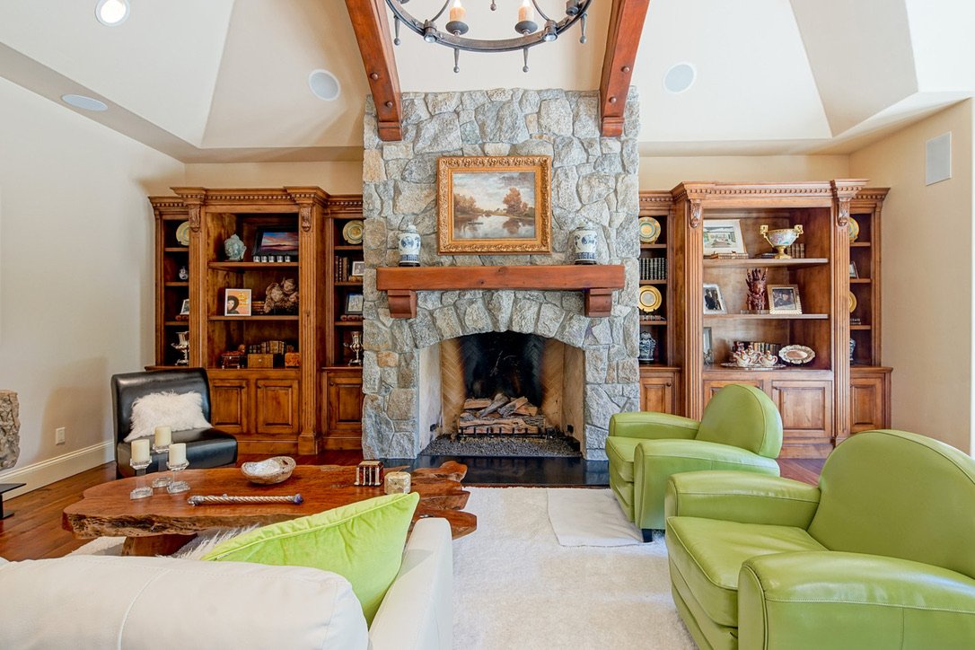 Living room with a stone fireplace, wooden bookshelves on either side, and green armchairs, a wooden coffee table, and decorative items.