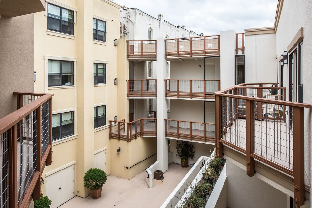 View of a multi-story residential building courtyard with several balconies with brown railings, potted plants, and windows on the walls.