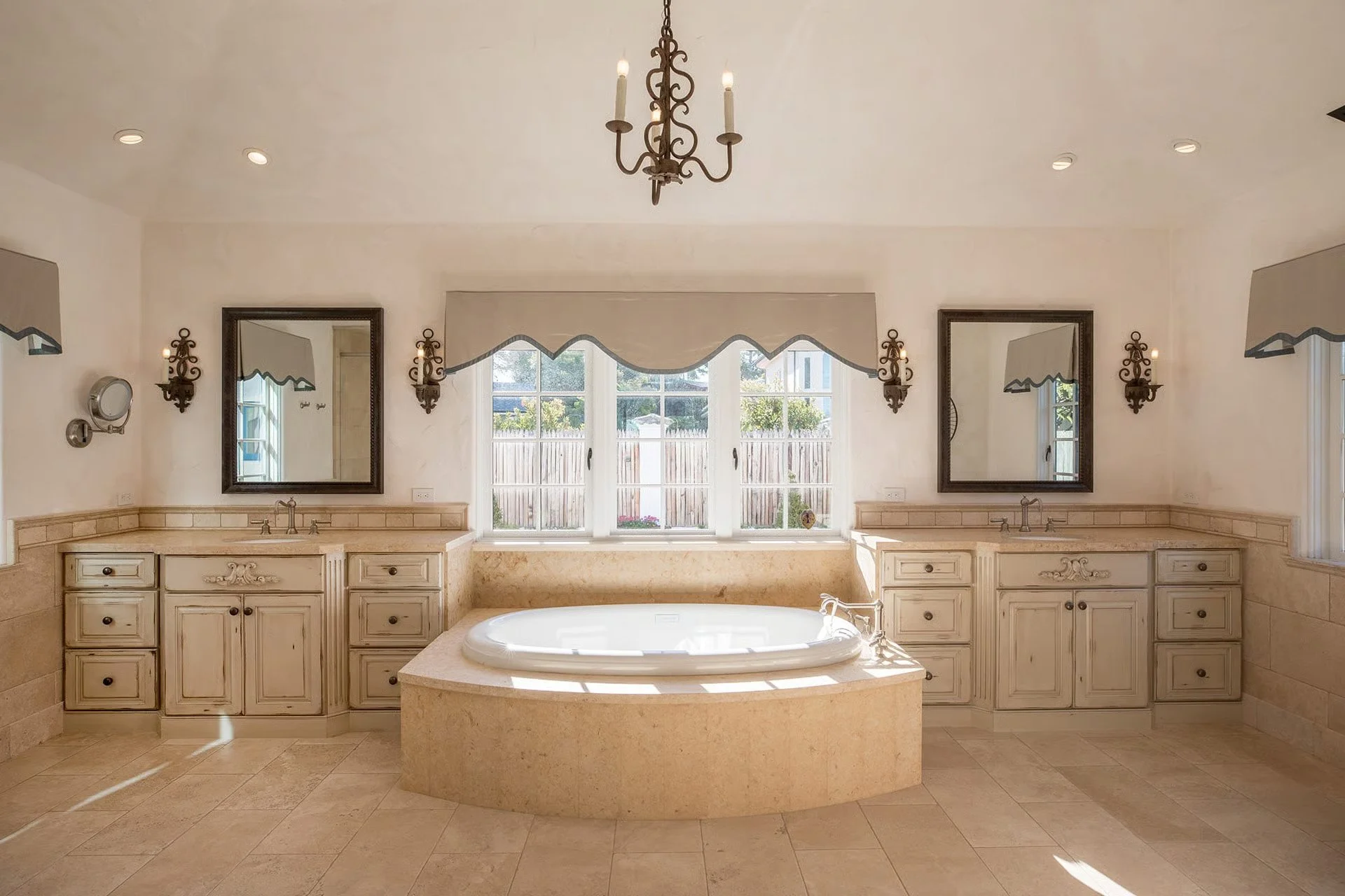 Bathroom with double sinks, large window, bathtub, and ornate mirrors and lighting fixtures.