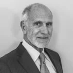Black and white portrait of an elderly man with a suit and tie, smiling slightly.