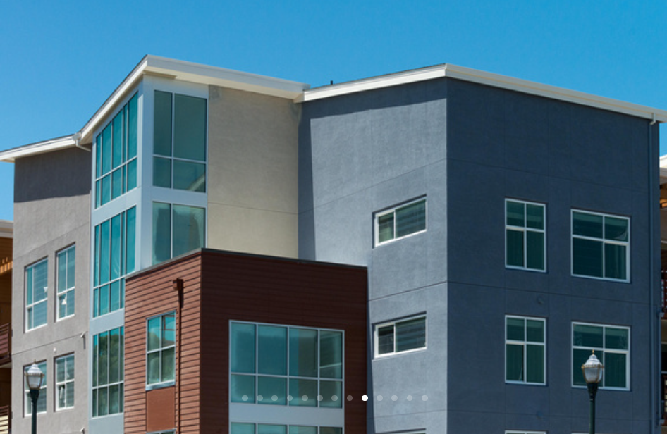 Modern multi-story apartment building with large windows, a blue sky, and street lamps in the foreground.