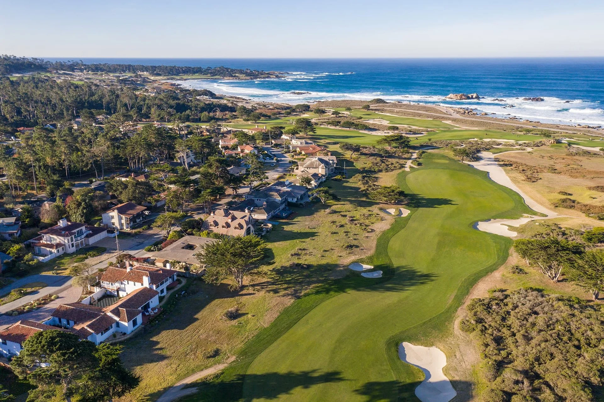 Aerial view of a coastal neighborhood with houses, a golf course, and the ocean in the background.