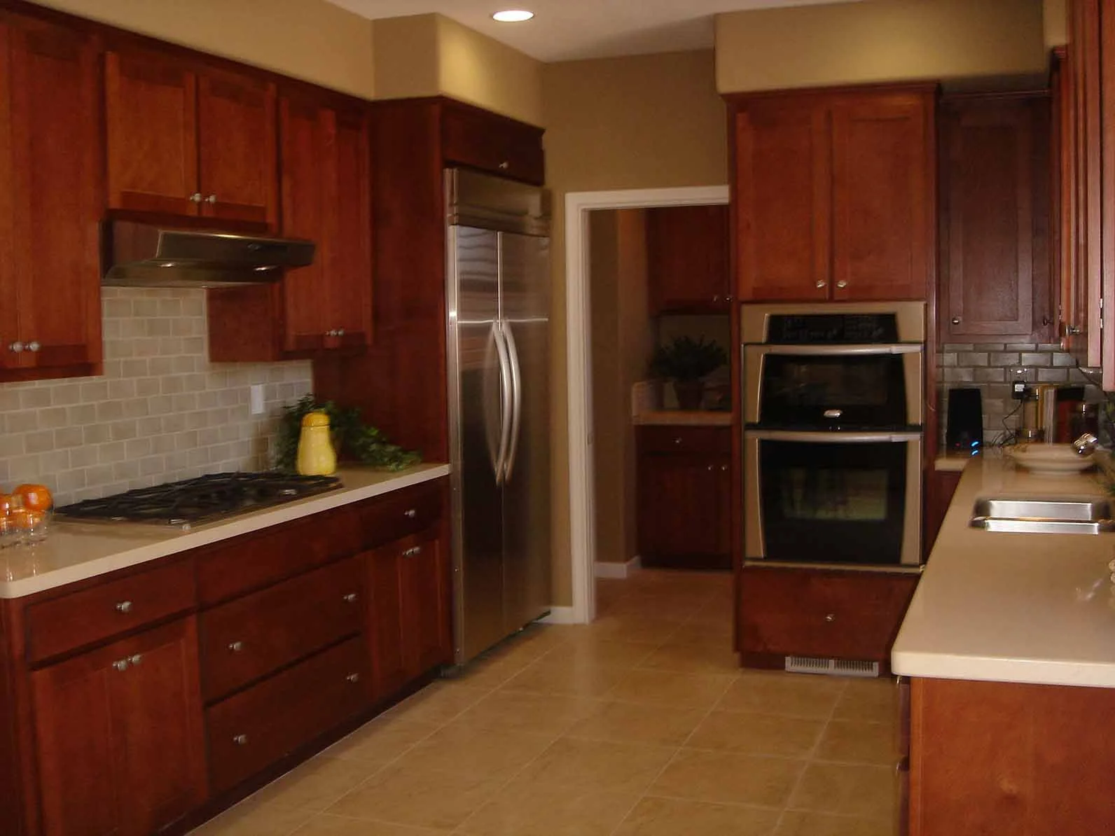 A kitchen with wooden cabinets, beige countertops, a tiled backsplash, a stainless steel refrigerator, a double oven, a gas stove, and a sink with a window above it.