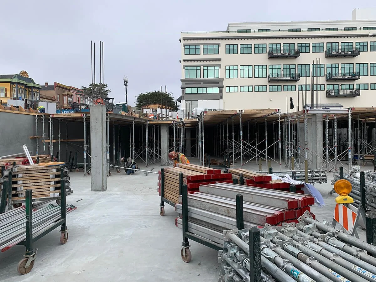Construction site with scaffolding, workers, and building materials in front of a multi-story building.