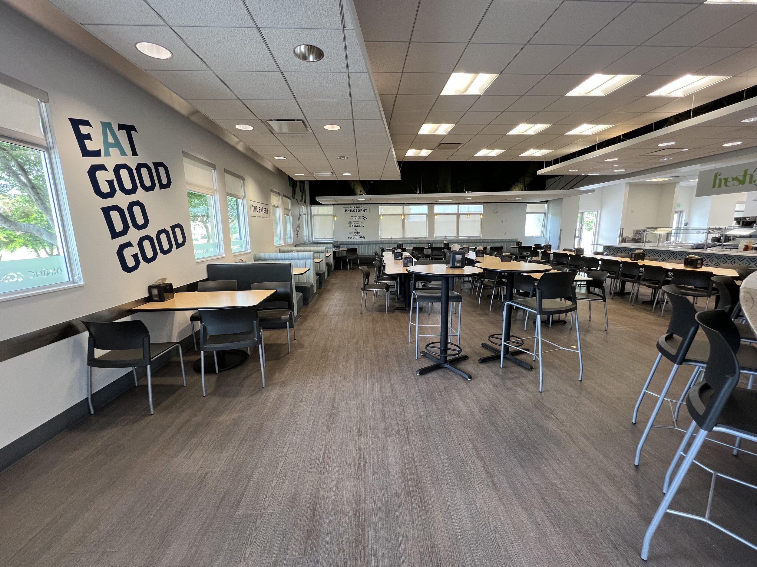 Empty restaurant dining area with windows, tables, chairs, and wall decor.