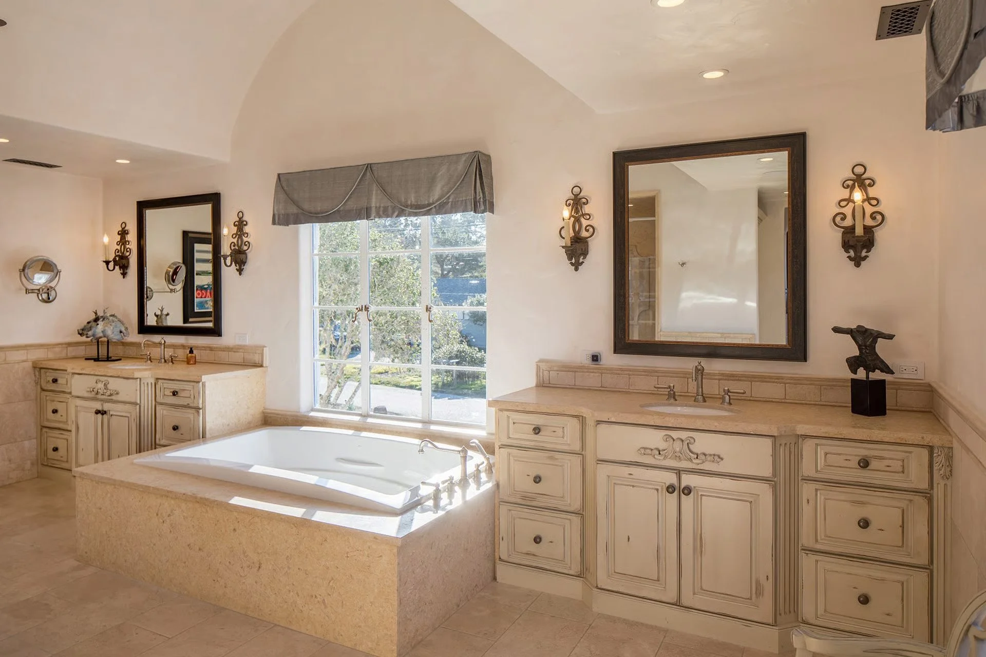 Bathroom with large bathtub, double sinks, large mirrors, and decorative wall sconces.