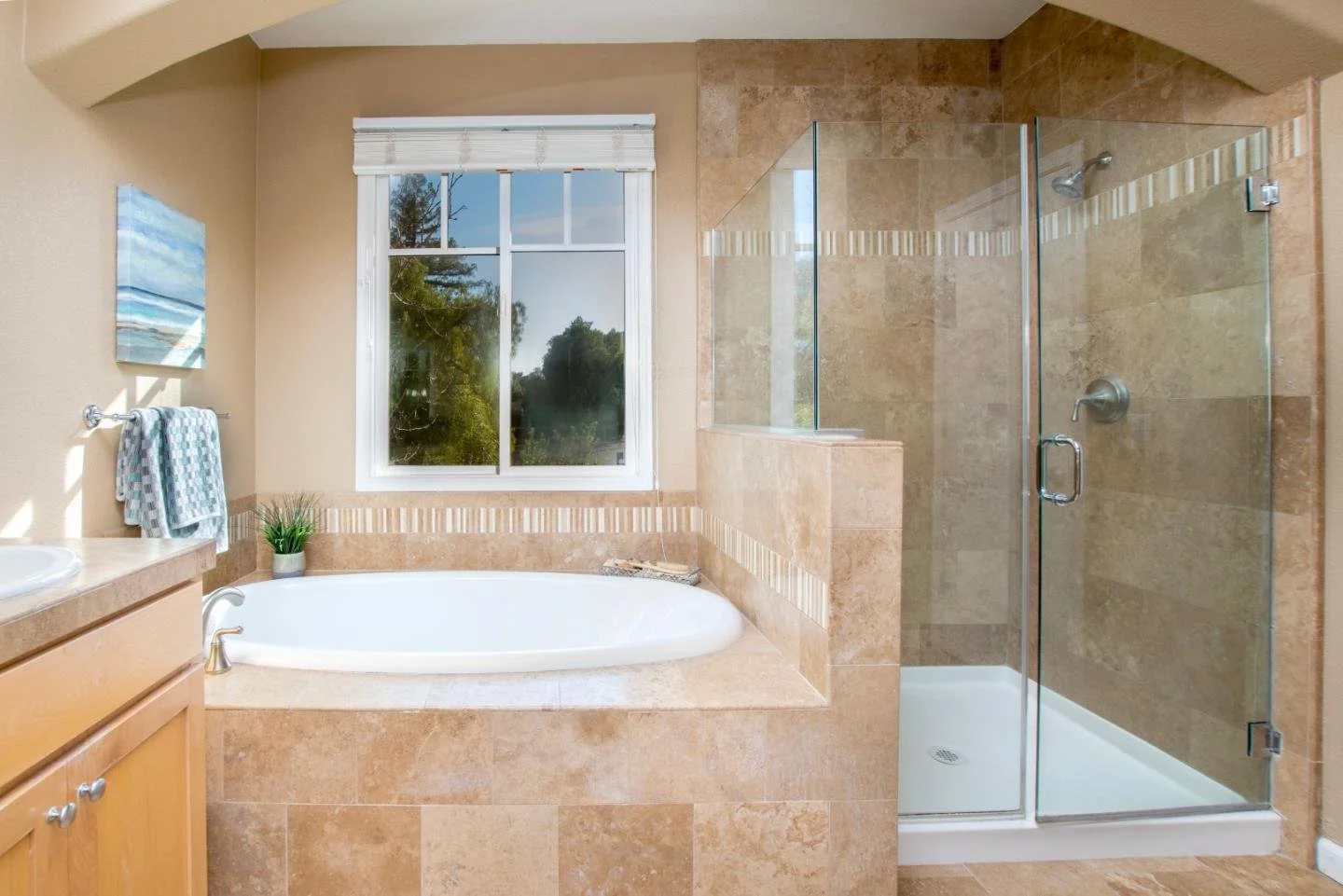 Bathroom with a bathtub, a window, a shower stall, and beige tiles.