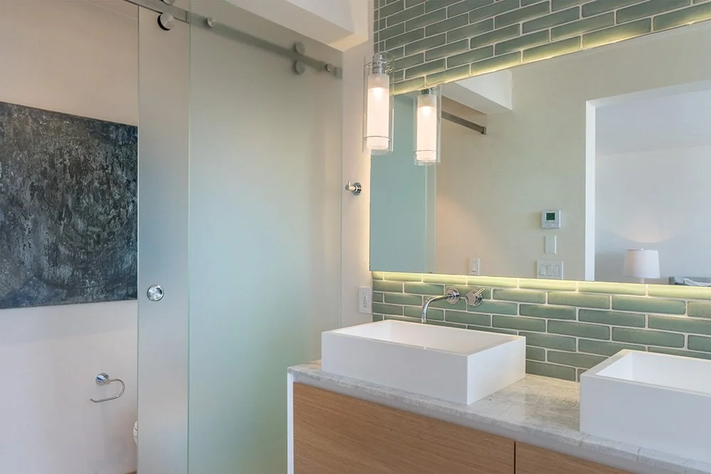 Modern bathroom with rectangular vessel sinks, a large mirror, green subway tile backsplash, pendant lights, and a neutral color scheme.