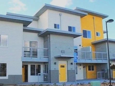 Colorful multi-story residential building with white, gray, and yellow exterior, balconies, and a handicapped parking sign in front.