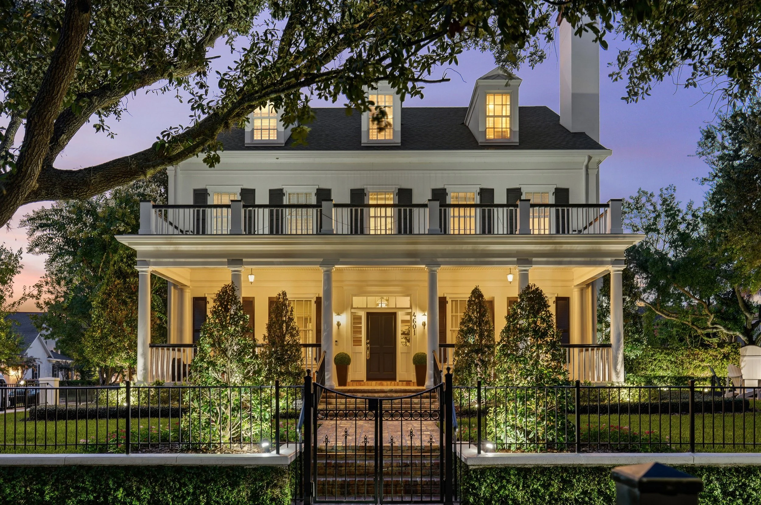 A captivating twilight view, with warm architectural lighting illuminating the grand covered porch and manicured grounds, while the mature oak canopy beautifully frames the home’s classic façade. 