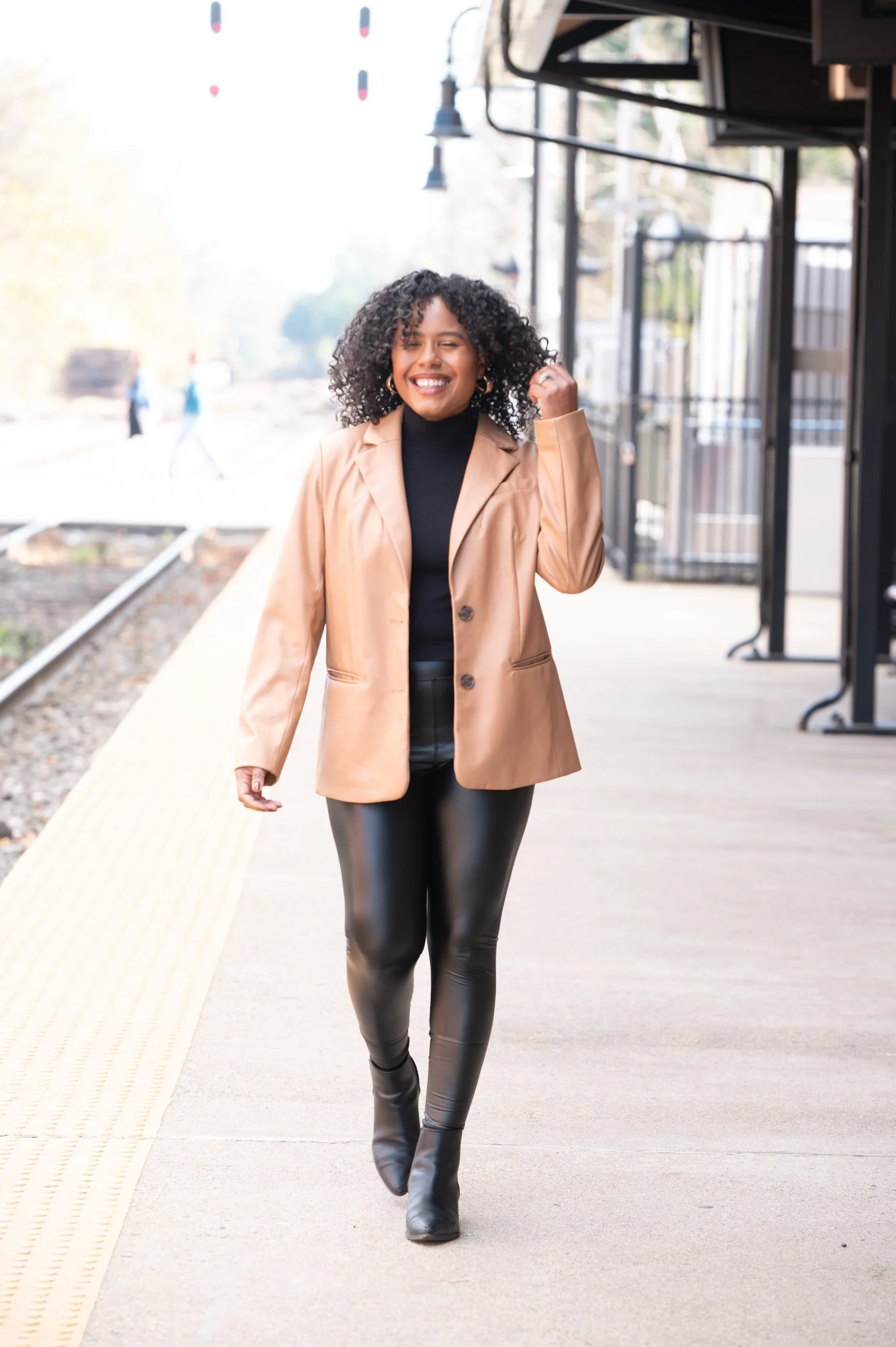 caroline wearing black leather leggings and brwon leather blazer walking along train platform
