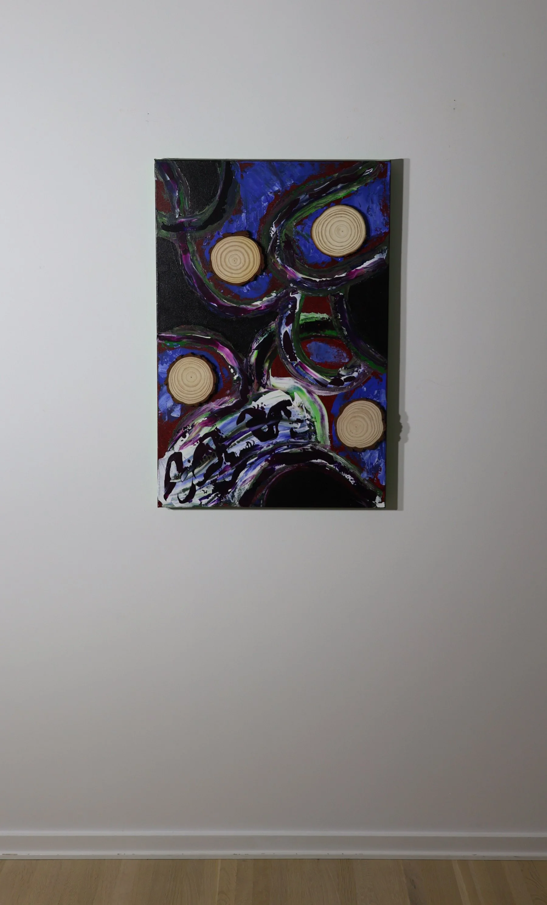 Abstract painting with colorful swirls and four wooden disks attached to the canvas, hung on a white gallery wall.