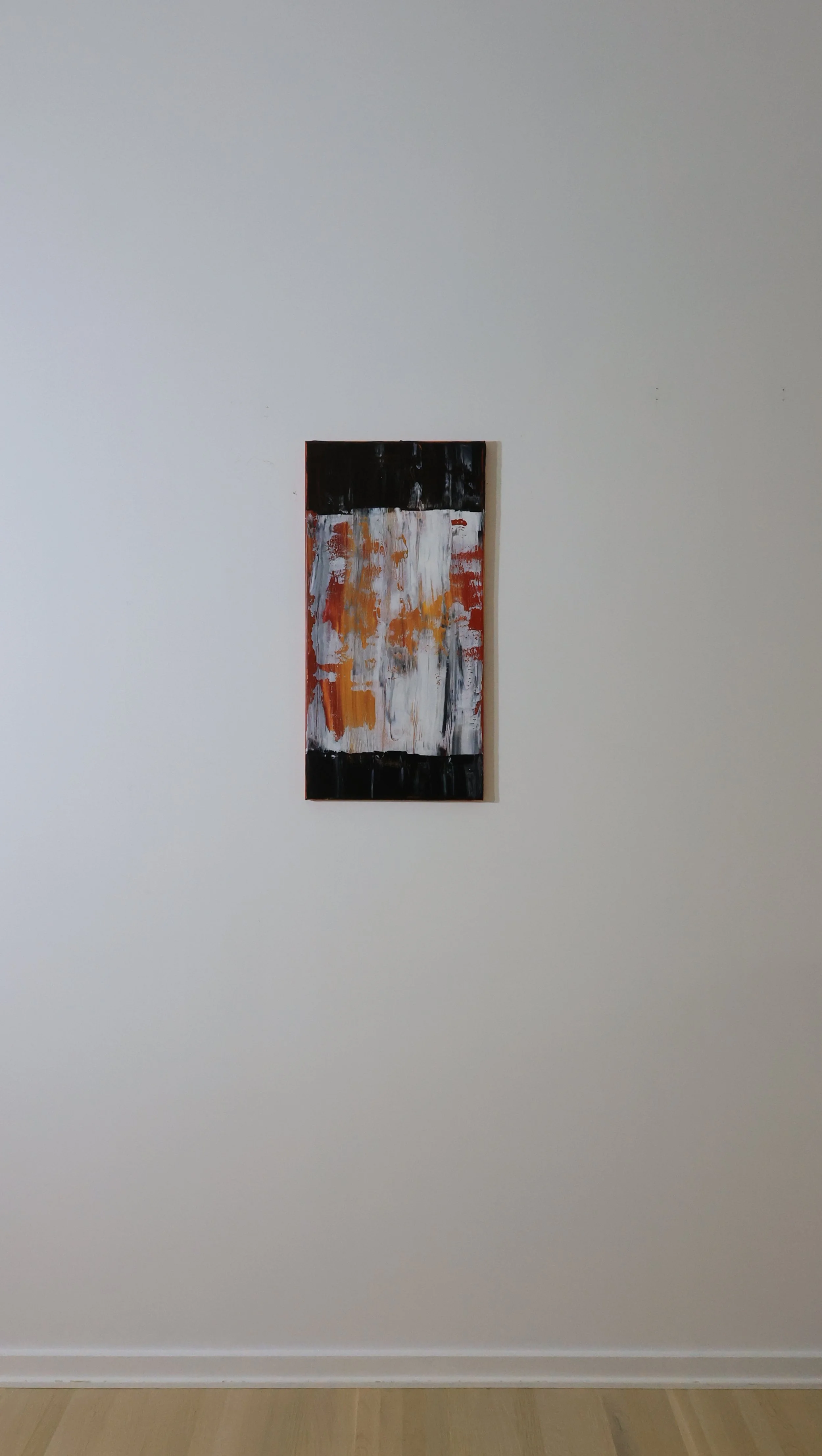 Abstract painting with black, white, orange, and hints of yellow on a small vertical canvas, hung on a plain white wall.