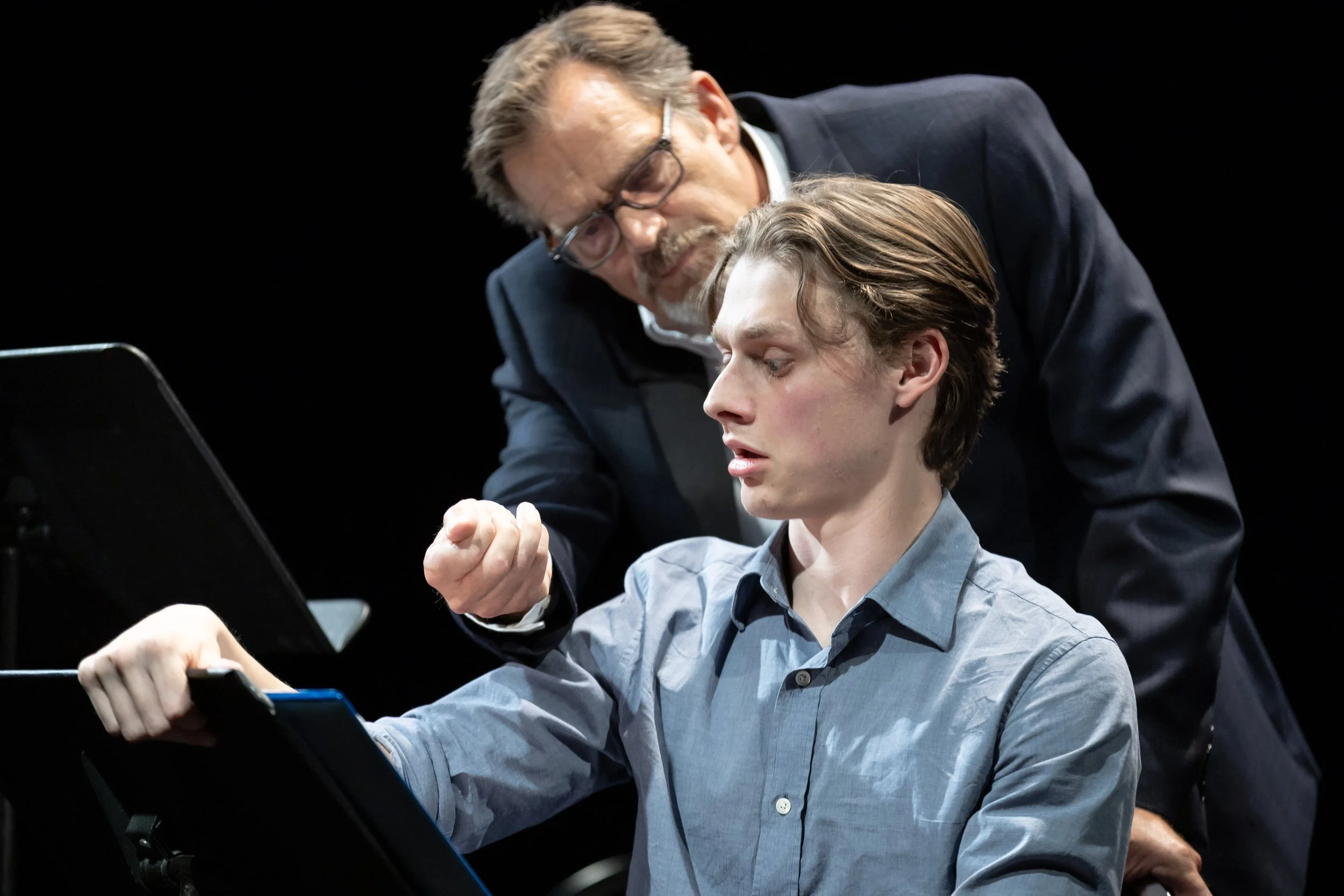 Two men stand around a music stand looking worried during a production of "The Picture of Dorian Gray"