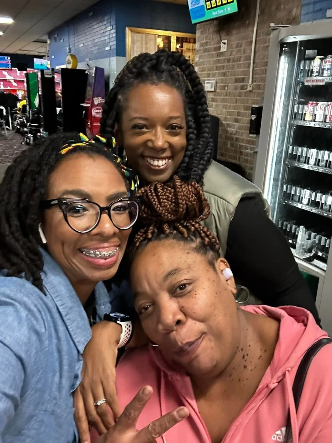 Three women taking a selfie together in an indoor setting with vending machines and arcade games in the background.