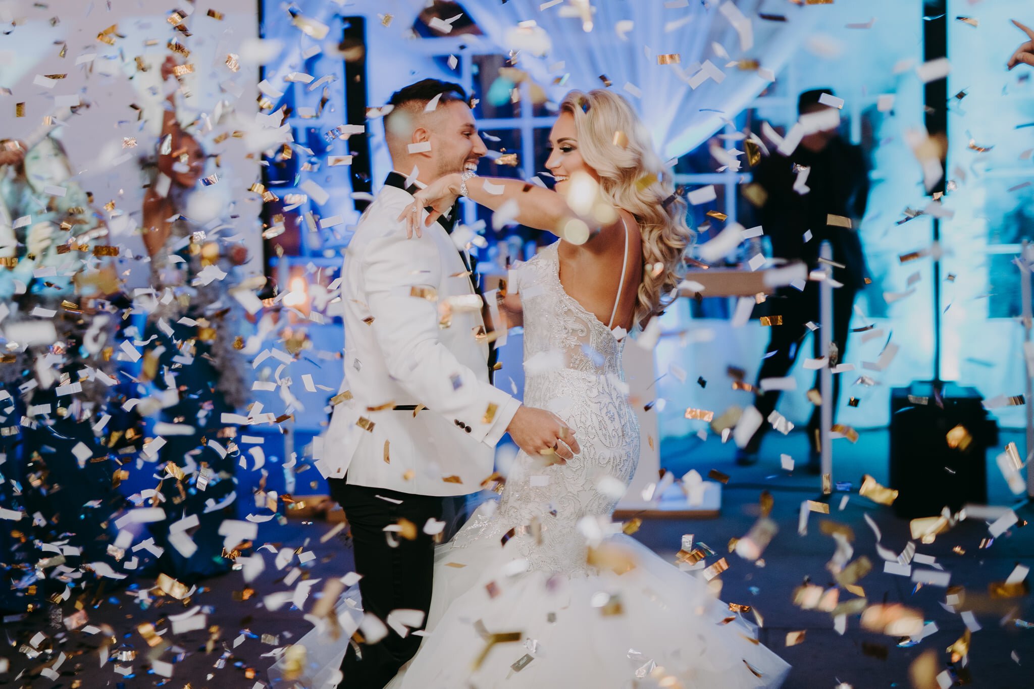 Bride and groom dancing amidst confetti at a wedding reception with a blue-themed decor.