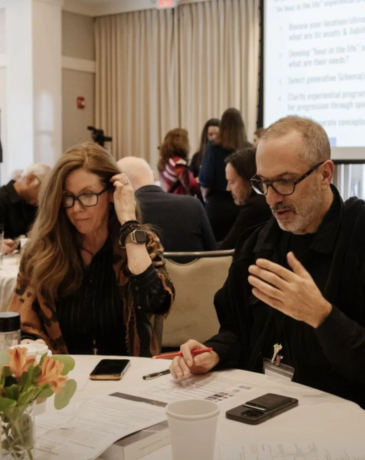 A mountain landscape with snow-capped peaks in the background and a modern building on a grassy hillside in the foreground.
