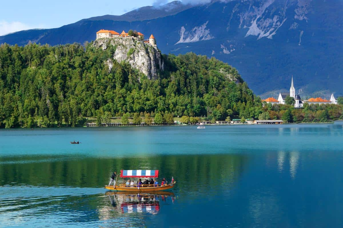 A boat in the foreground while castles and chapels are shown in the background of a picture of Lake Bled, Slovenia