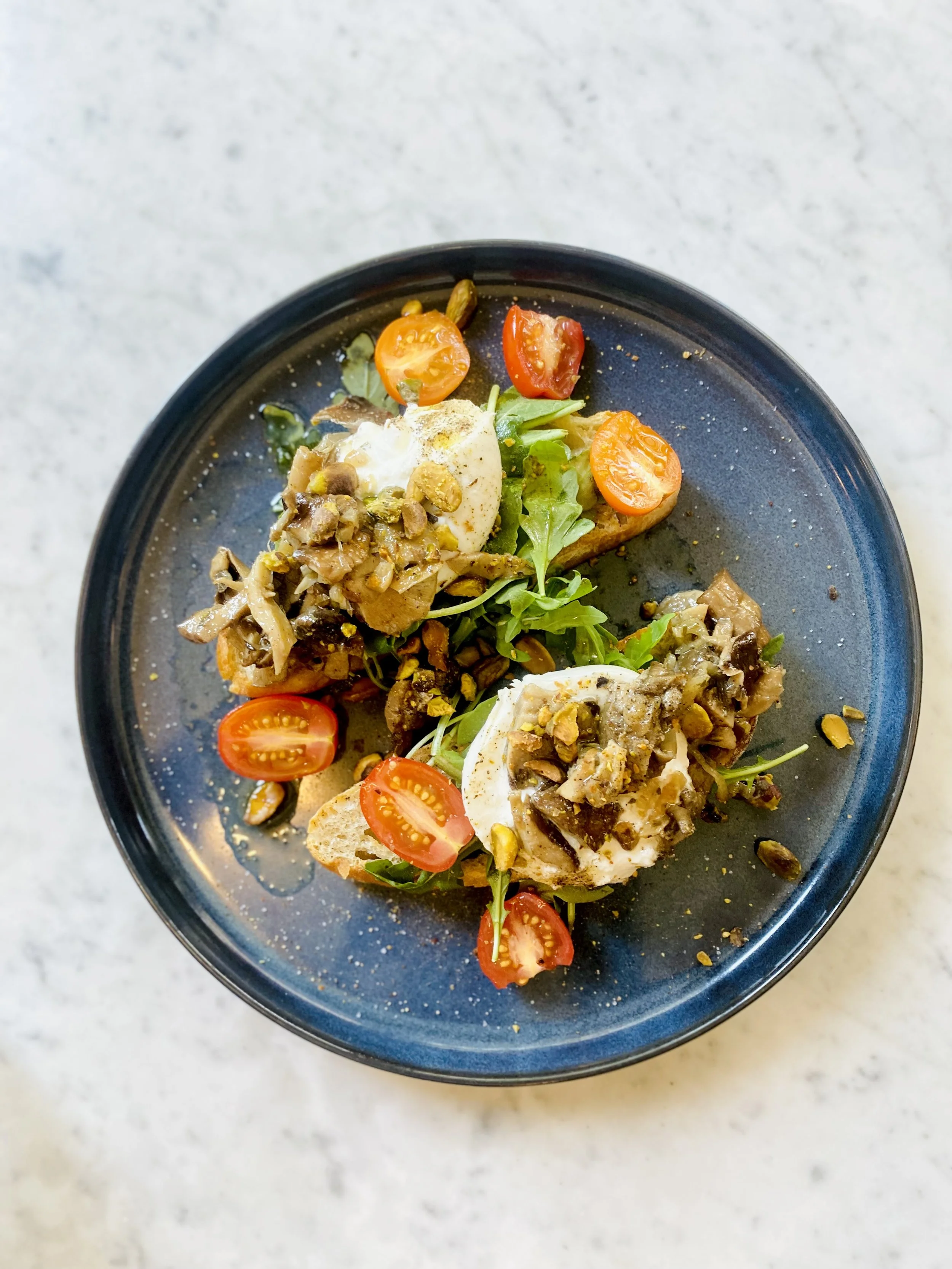 Salade avec œufs mollets, tomates cerises, champignons et pistaches sur une assiette noire.