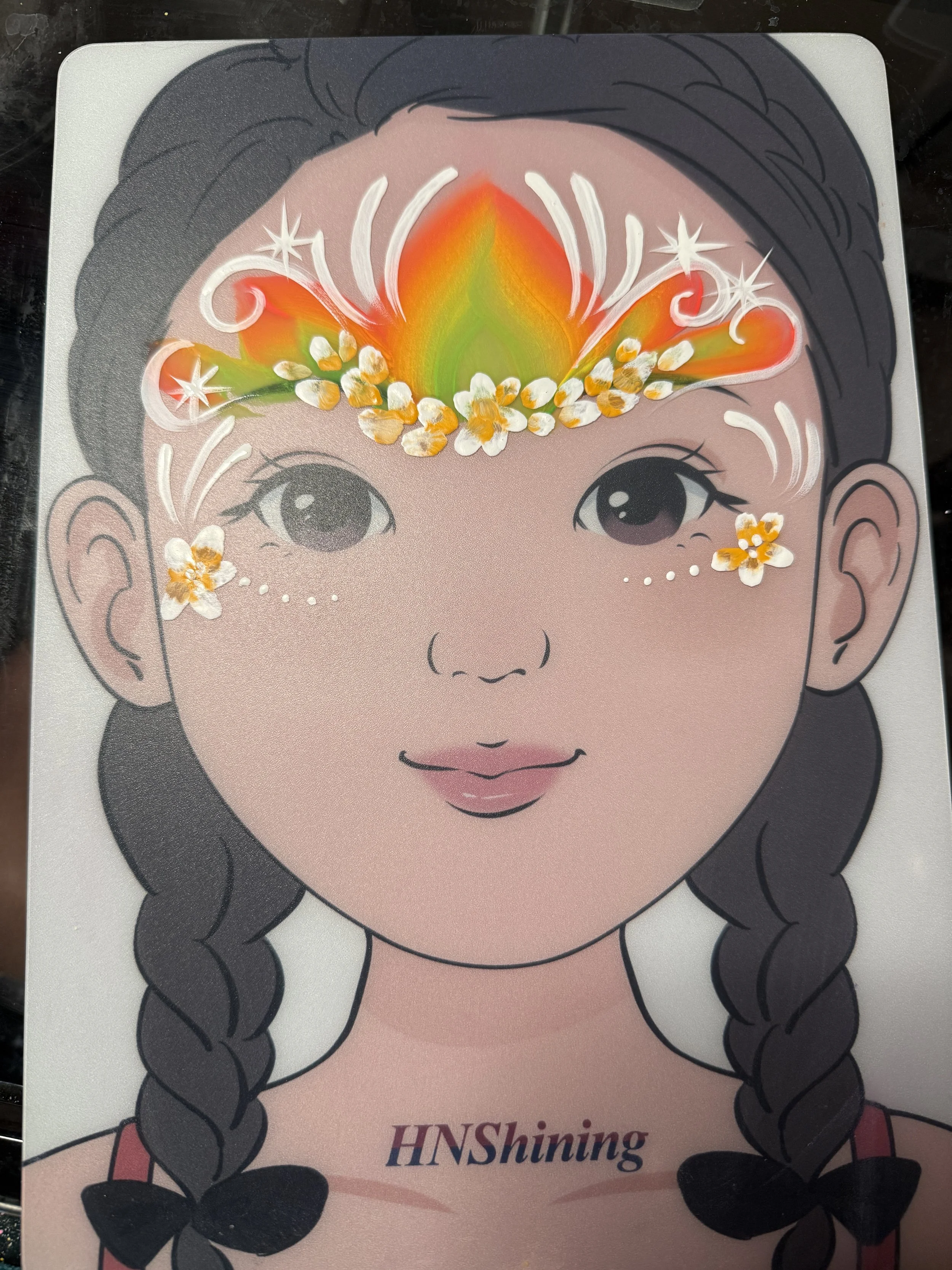 A cartoon illustration of a girl's face with braided hair, featuring a colorful flame design on her forehead surrounded by white decorative elements and small white flowers, with text that says 'HNShining' underneath.