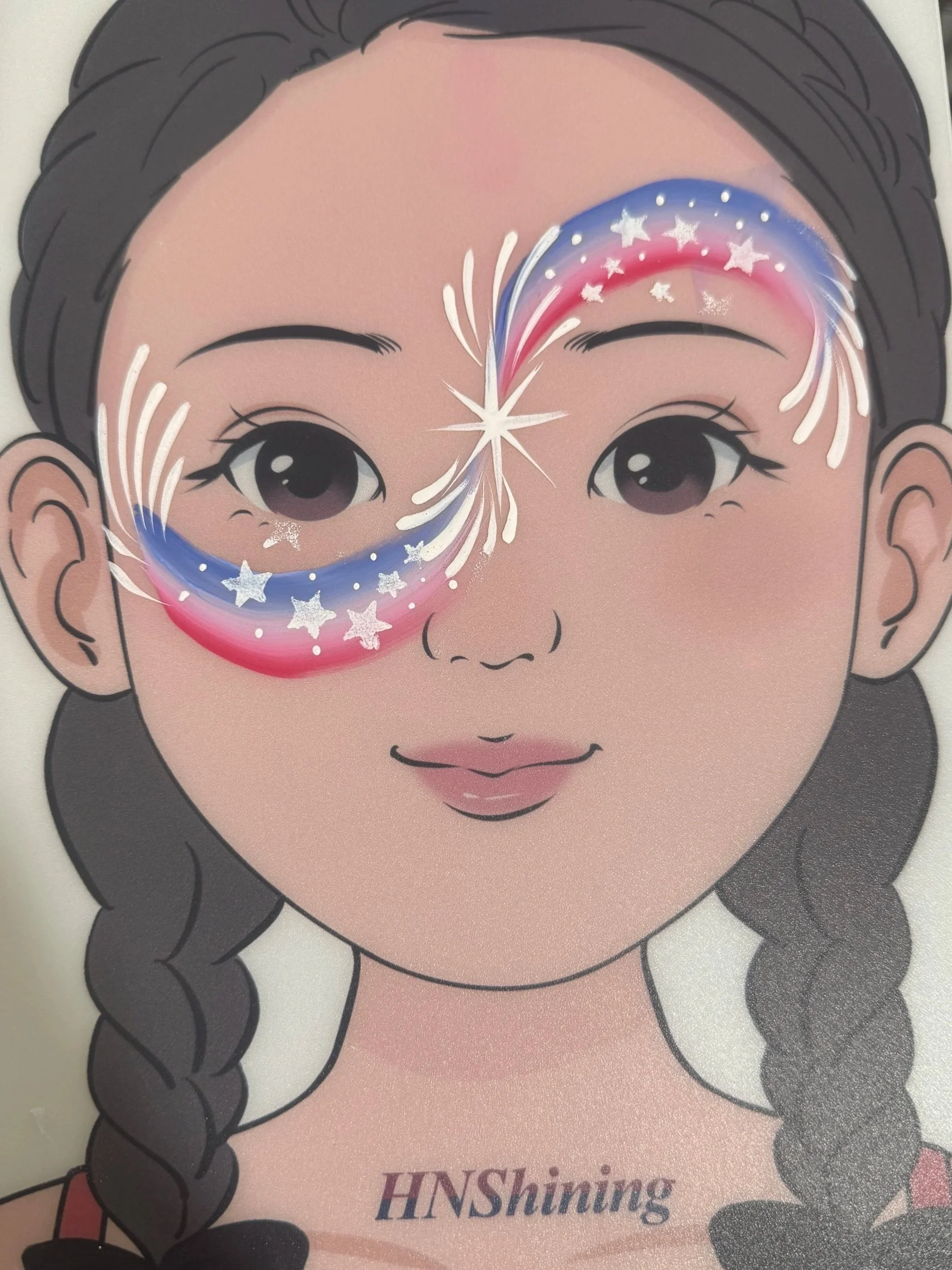An illustration of a child's face with two braided hair pigtails, large eyes, and pink cheeks. The child has a creative face paint design around the eyes, featuring stars, white lines, and a swirl of color in blue, red, and white. The text 'HNShaing' is printed at the bottom of the illustration.