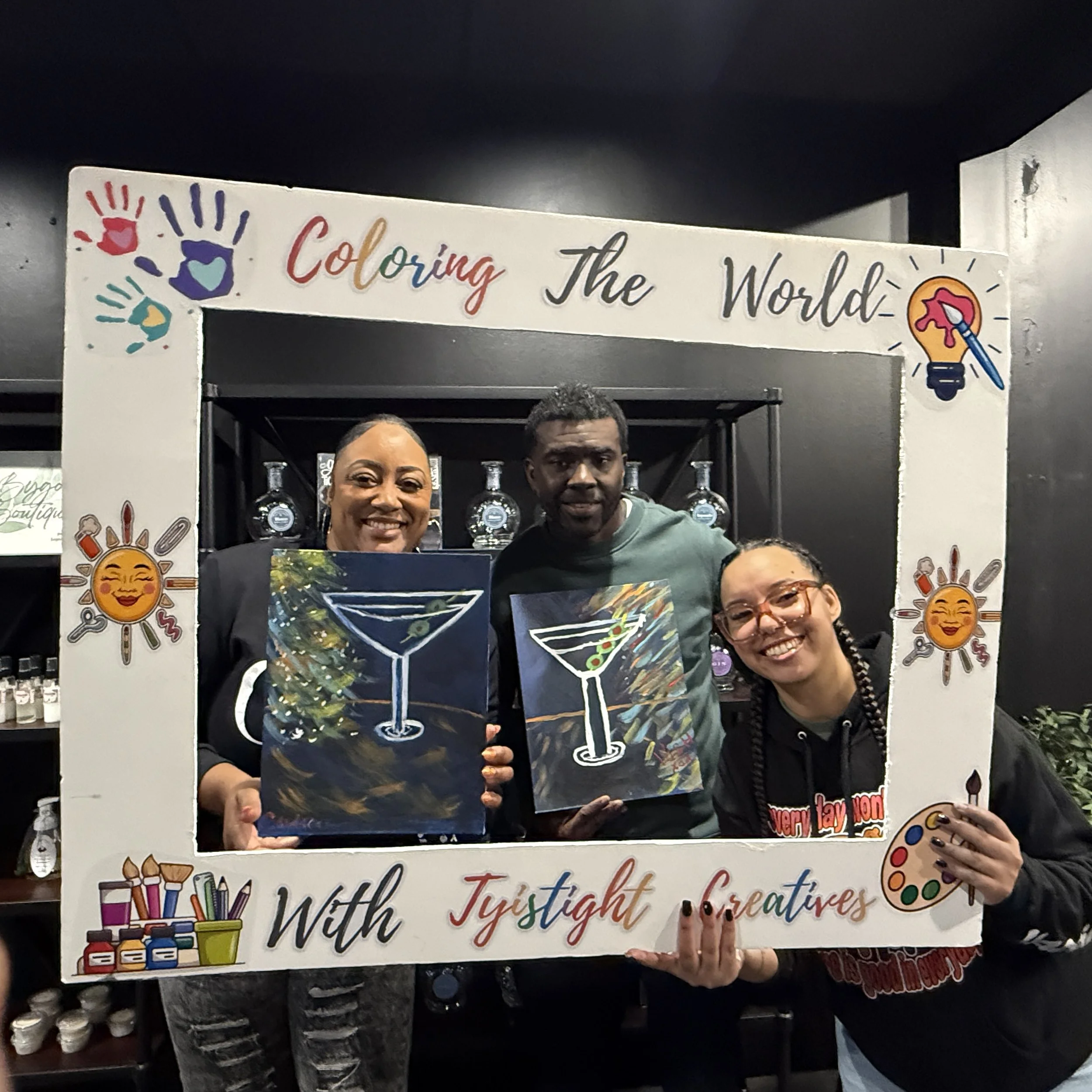 Group of people standing behind a sign that says, 'Coloring the World with Justight for Creatives,' with colorful illustrations of art supplies and decorations.