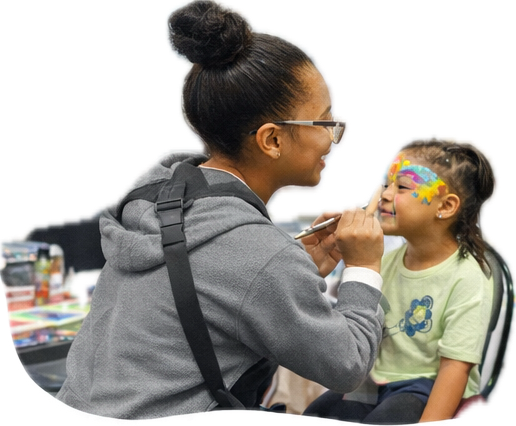 A woman is painting colorful face art on a young girl's face during a fun activity.