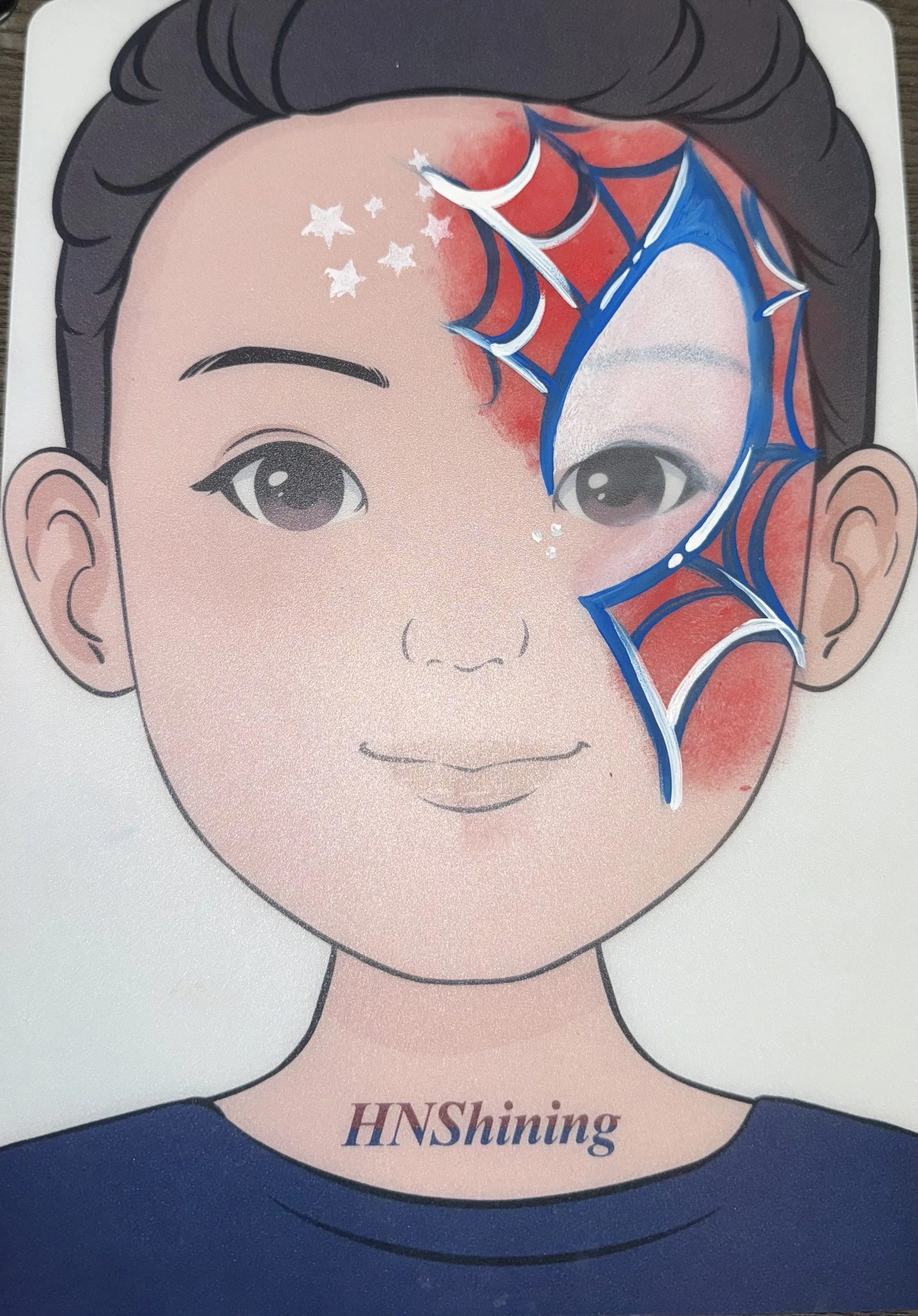 A cartoon illustration of a young person's face with dark hair, light skin, and glasses. The face has a red, star, and moon design on the forehead and right eye, with the star and moon appearing to be part of a decorative face paint or mask. The person is wearing a blue shirt with the partially visible text "HNShining".