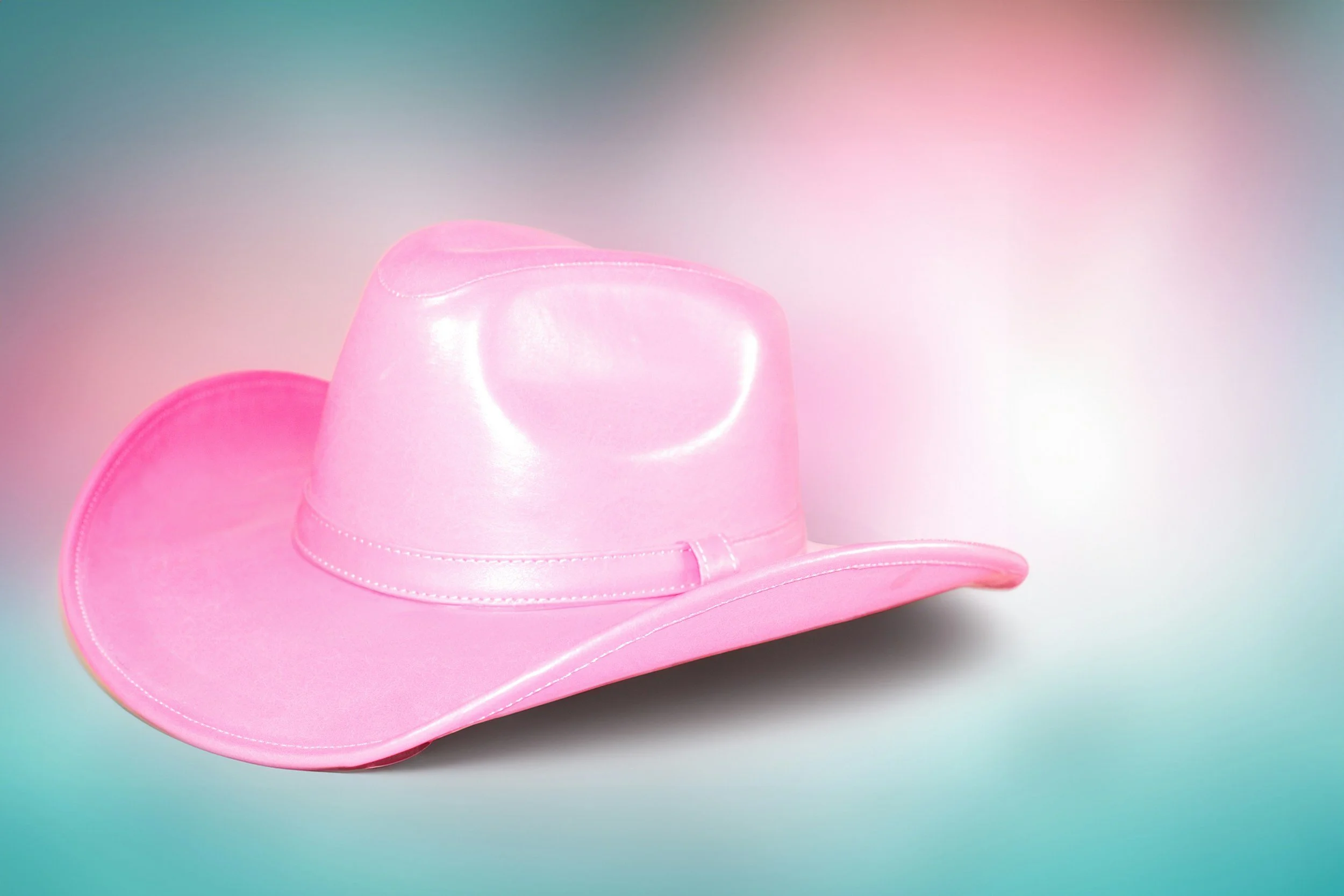 Pink cowboy hat with a wide brim on a pastel gradient background.