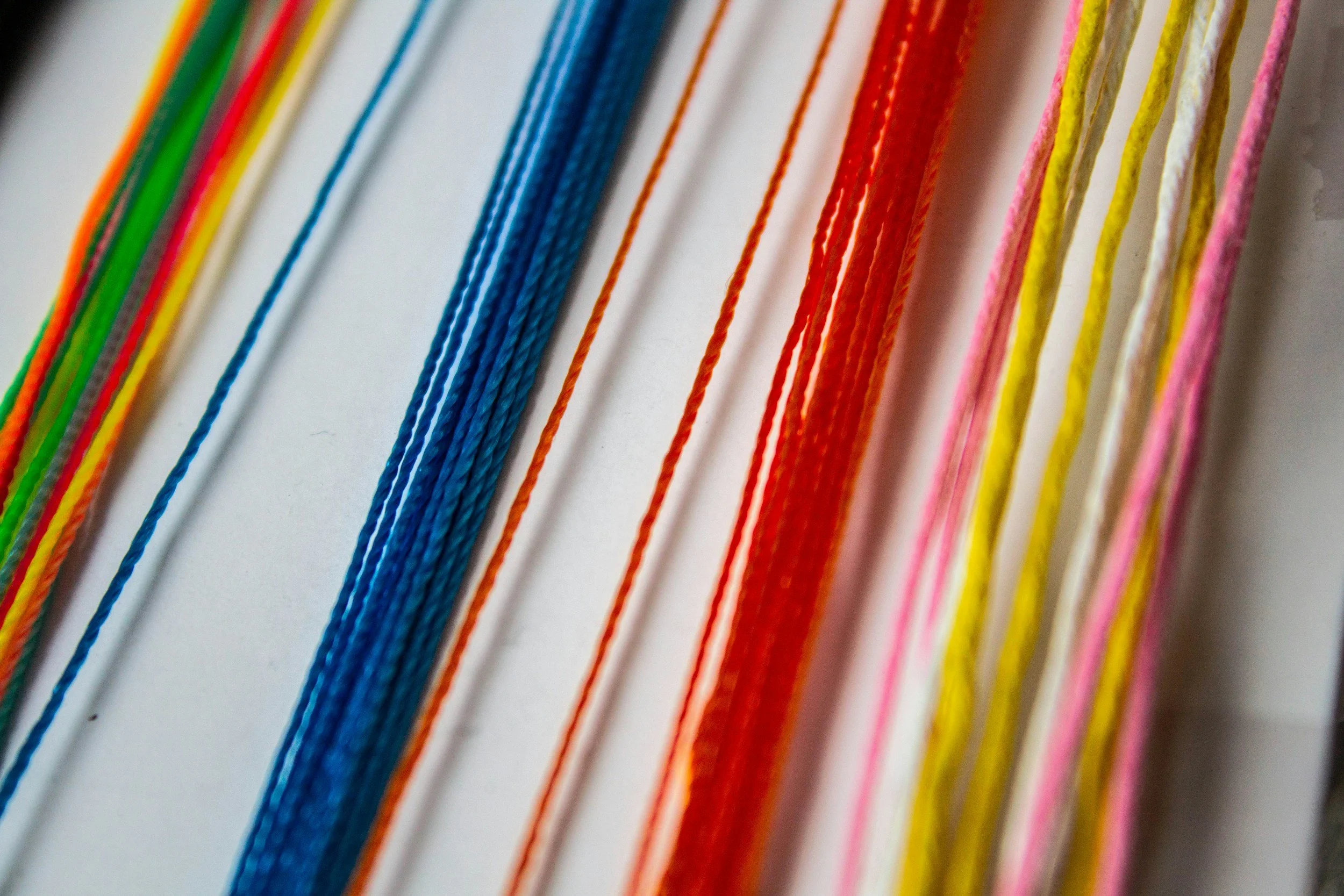 Close-up of colorful strings or threads arranged in a row, including green, yellow, blue, red, orange, pink, and white colors.